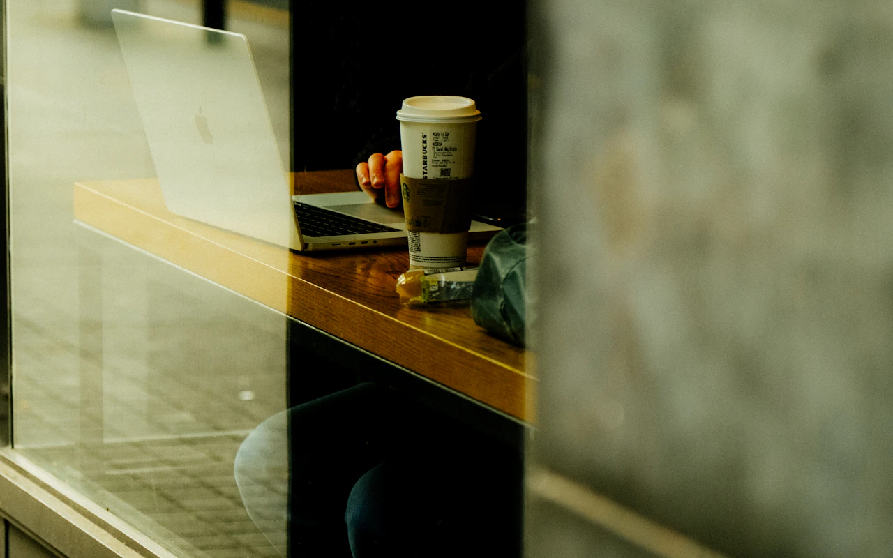 A person concentrating on a laptop beside a cafe window.