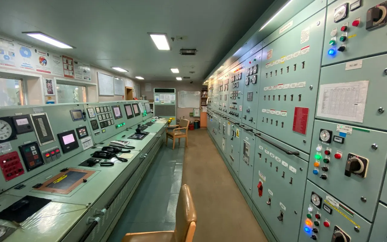 The engine control room of a ship, with a long console of gauges and switchboards along one wall.